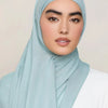 Une femme portant un foulard modal bleu clair avec une tenue blanche.