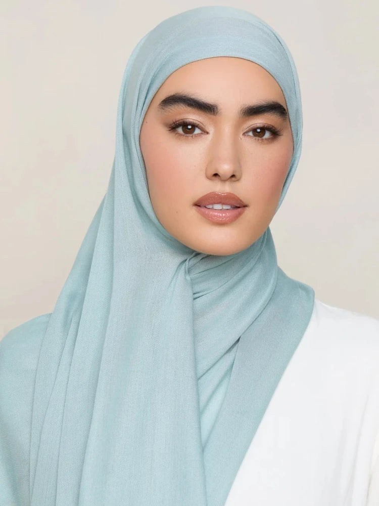 Une femme portant un foulard modal bleu clair avec une tenue blanche.