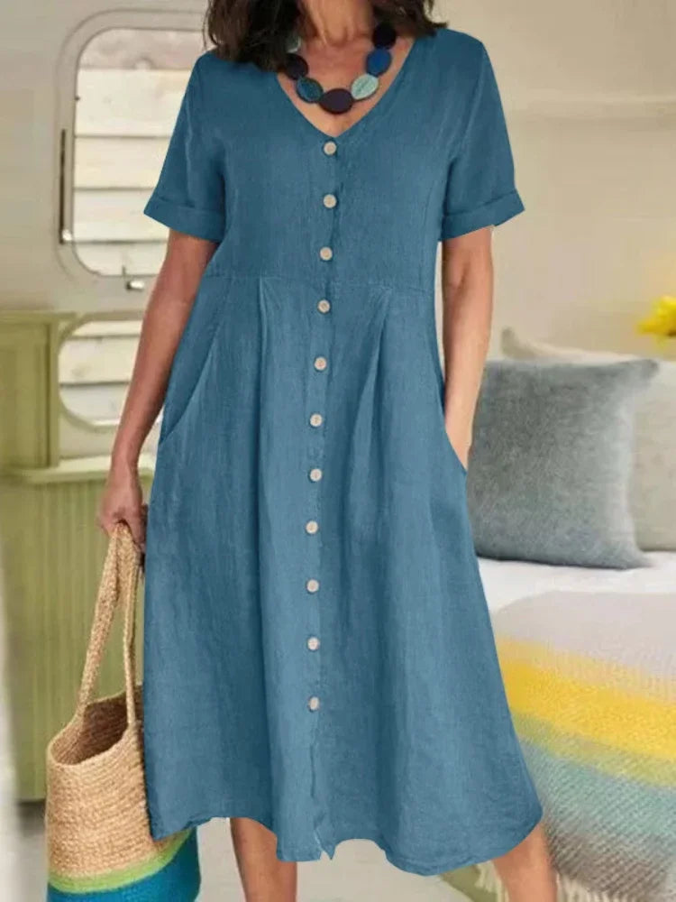 Eine Frau präsentiert ein staubiges blaues Baumwoll- und Hanf-V-Ausschnittkleid mit kurzen Ärmeln und Knöpfen.
