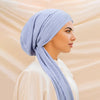 A woman wearing a light blue striped turban hijab cap and a cream-colored top.