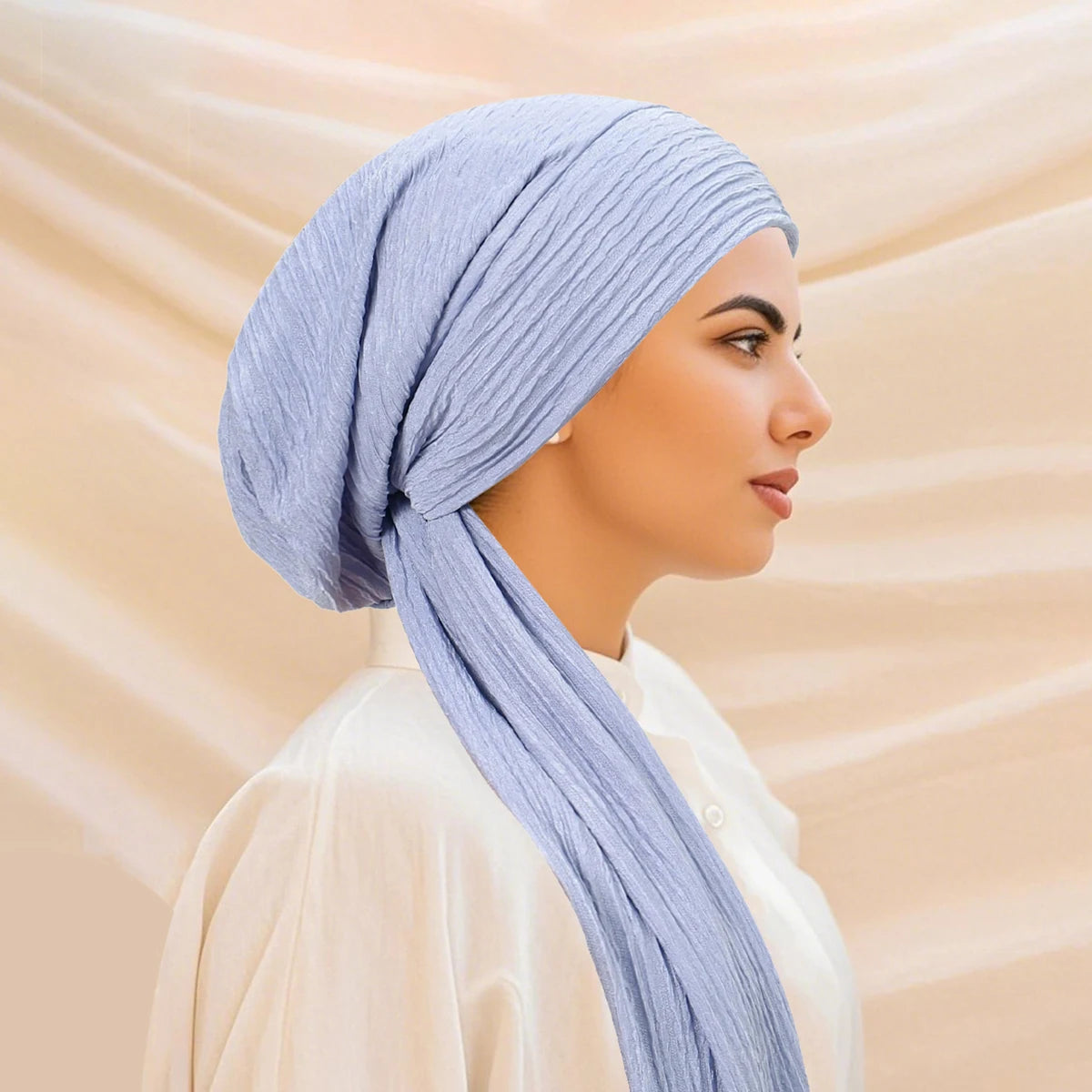 A woman wearing a light blue striped turban hijab cap and a cream-colored top.