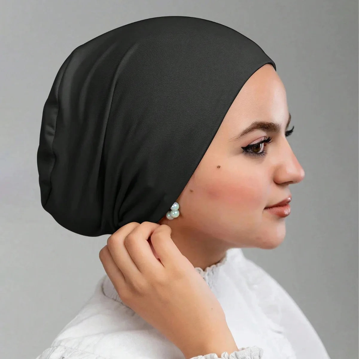Una mujer vistiendo una gorra interior de jersey negro elástica con un pendiente de perla.