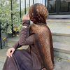 Eine Frau mit braunem Hirschmuster-Hijab-Schal sitzt auf Steinstufen im Freien.