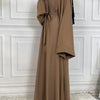 Eine Frau trägt eine elegante, bodenlange braune Maxi-Abaya mit schwarzem Zier und einer Gürtelverzierung.