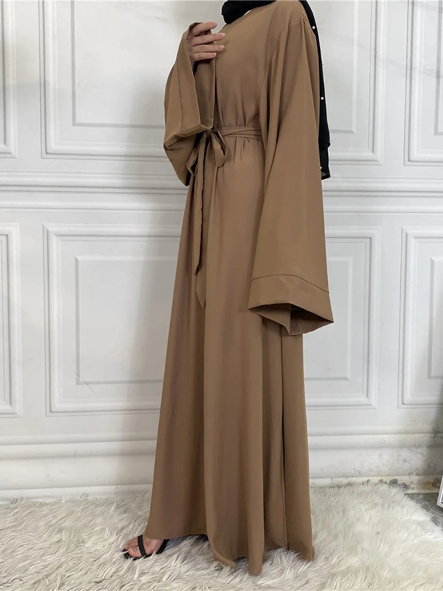 Eine Frau trägt eine elegante, bodenlange braune Maxi-Abaya mit schwarzem Zier und einer Gürtelverzierung.