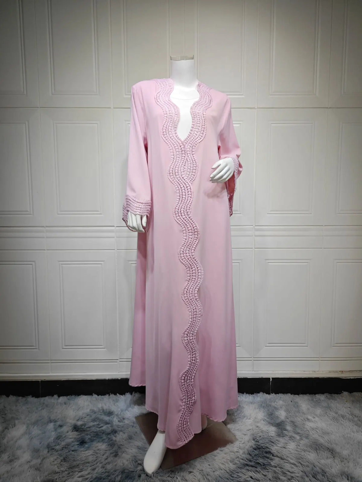 Vestido caftan maxi rosa elegante exhibido en maniquí contra pared de paneles blancos.