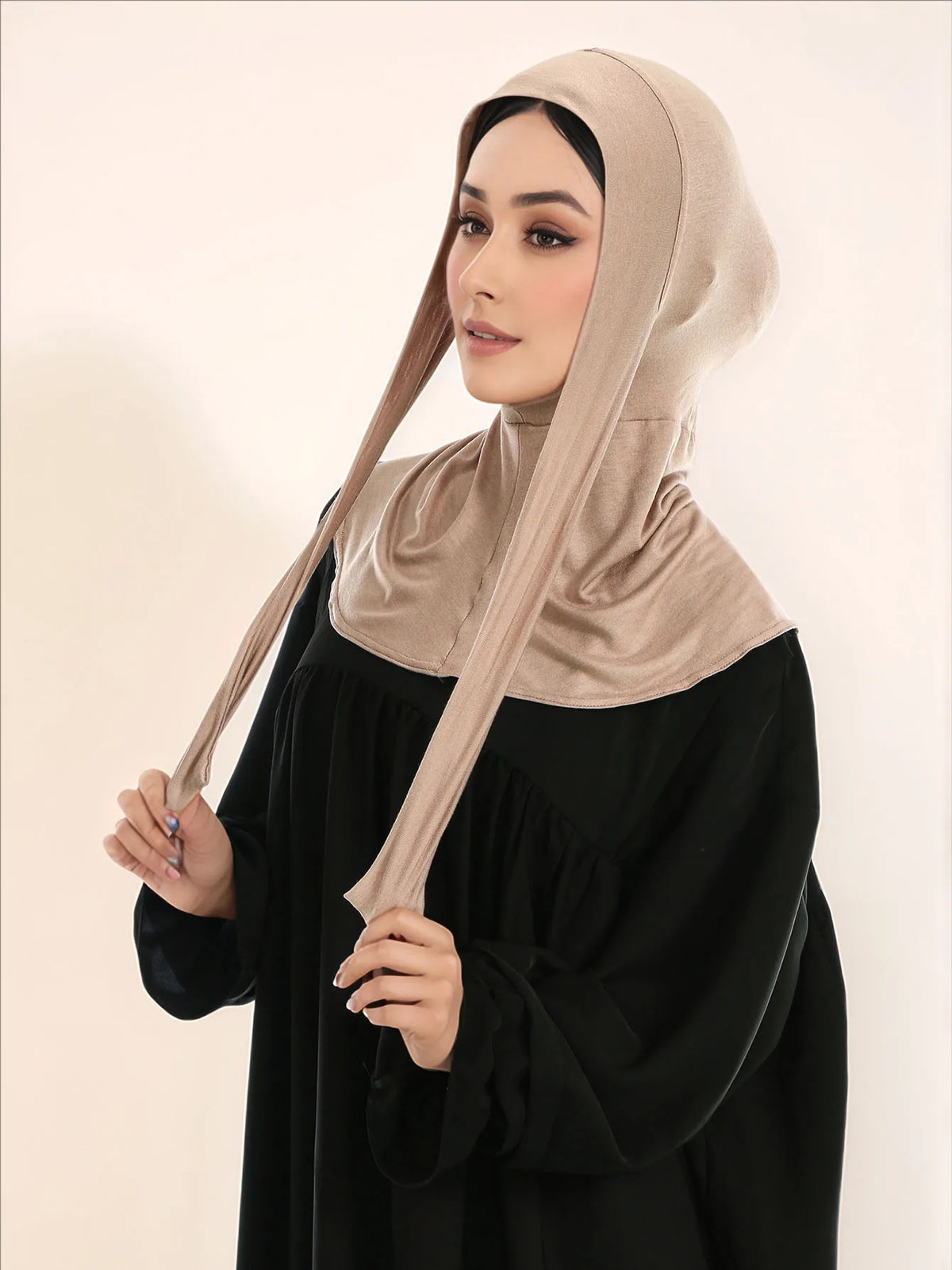 Una mujer vistiendo un hijab beige de cobertura total con un lazo sobre un vestido negro.