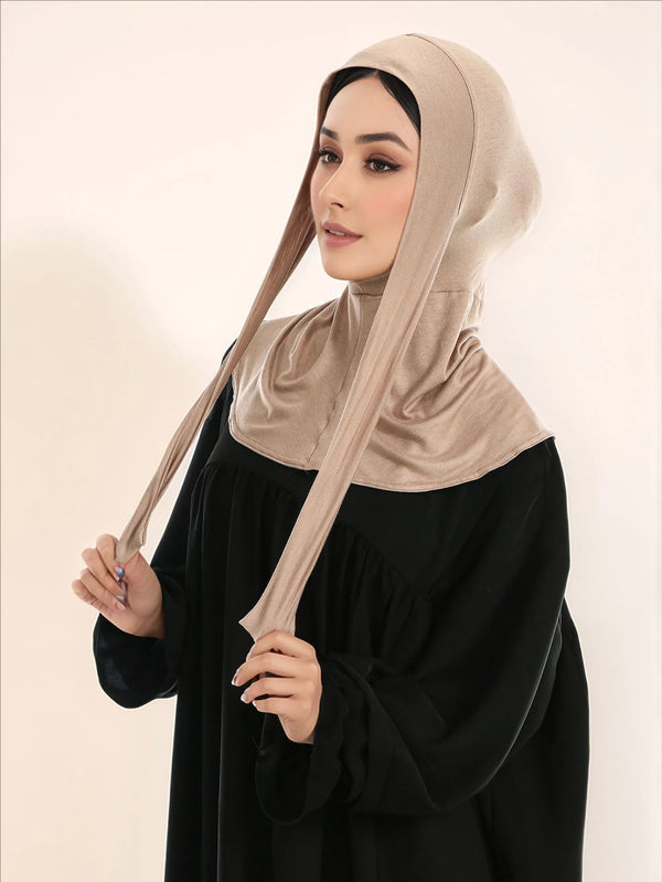 A woman wearing a beige full coverage hijab with a tie-back over a black dress.