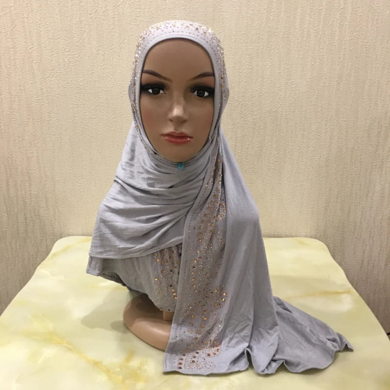 Un modèle porte une écharpe de jersey gris doux avec des embellissements en cristal drapée sur sa tête et ses épaules.