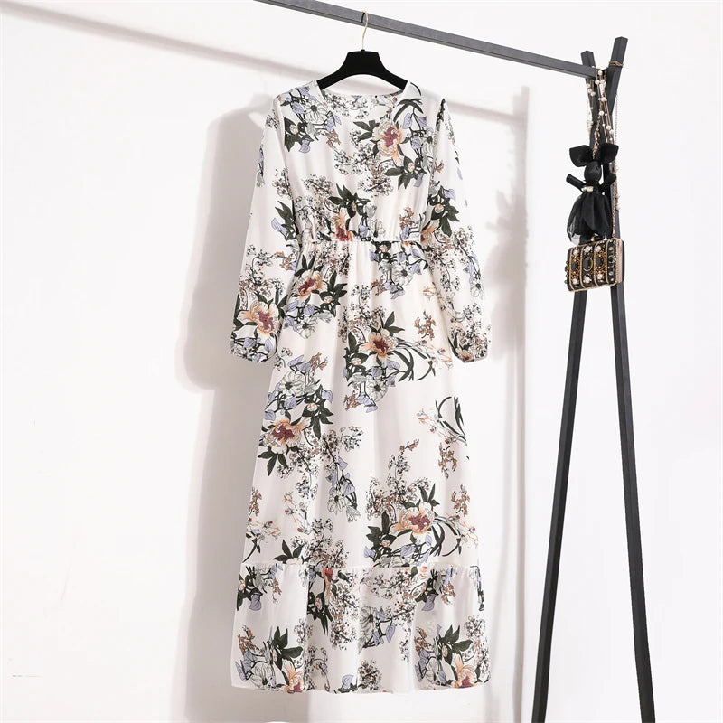 Weißes Maxi-Kleid mit Boho-Blumenmuster an einem schwarzen Haken vor weißer Wand.
