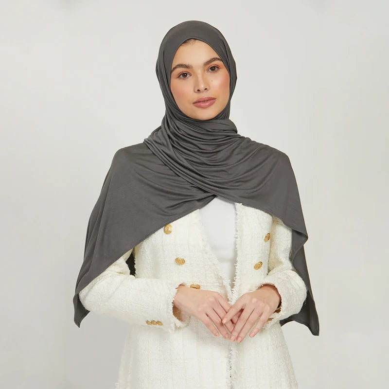 A woman wearing a gray stretchy jersey plain hijab scarf and a white jacket.