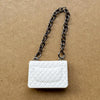 Bolso de cuero acolchado blanco con cadena de plata, fotografiado sobre una superficie marrón.