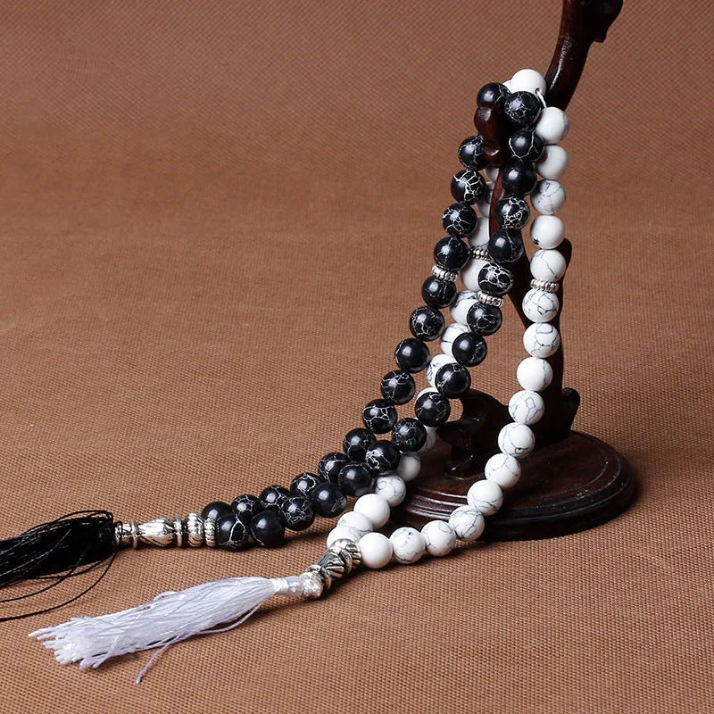 A necklace featuring black and white agate prayer beads strung on a dark wooden cord with a white tassel.