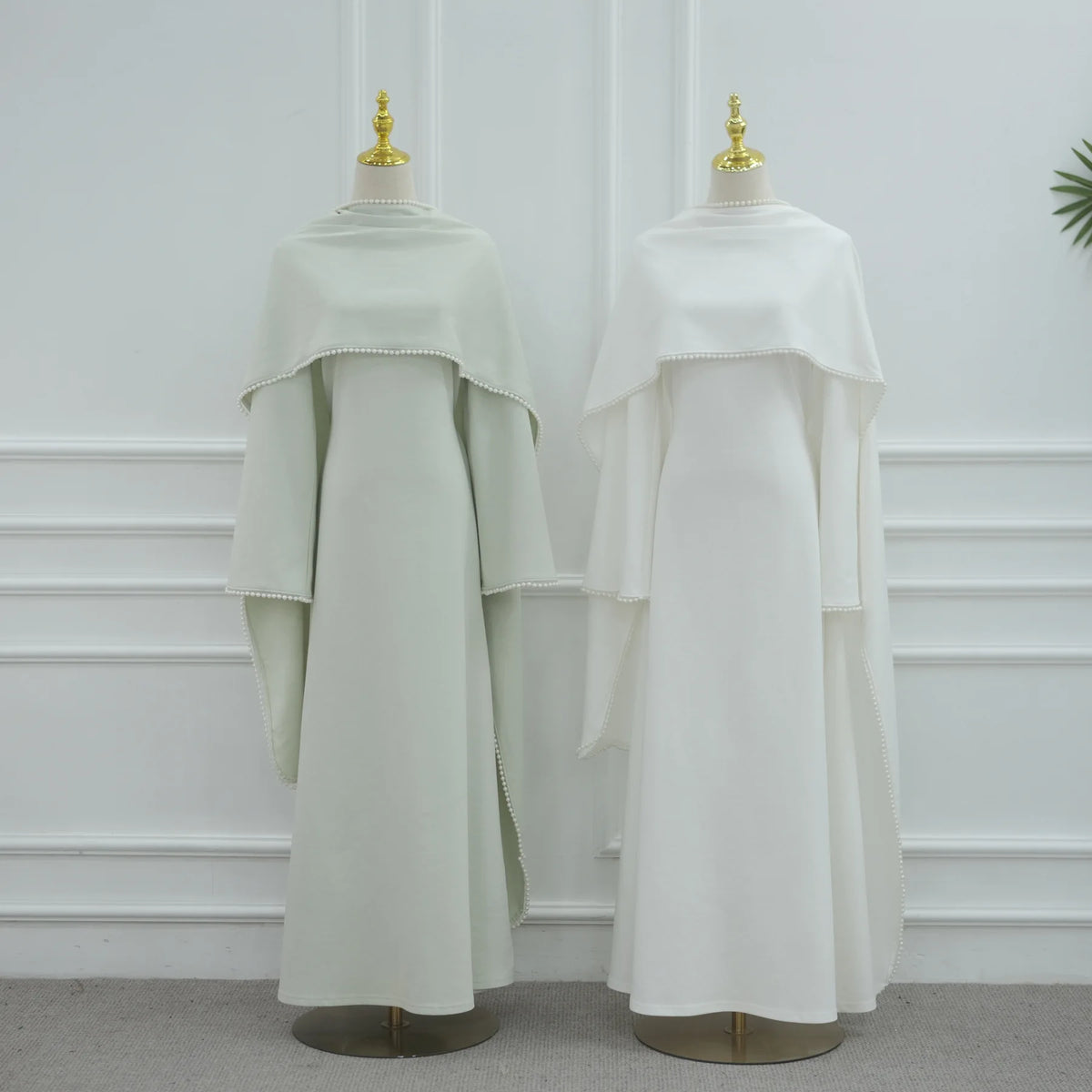 Langes, gedecktes salbeigrünes, einfaches Abaya-Kleid auf einem Mannequin vor einer weißen Wand.
