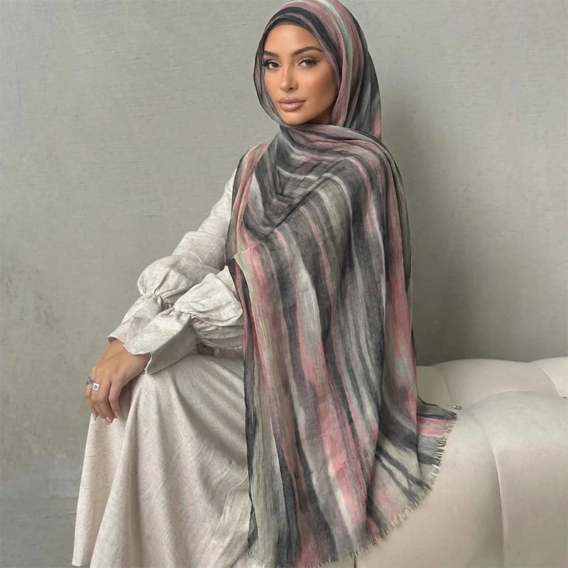 Una mujer vistiendo un pañuelo hijab floral de acuarela bohemio rayado en gris y rosa y un conjunto a juego.