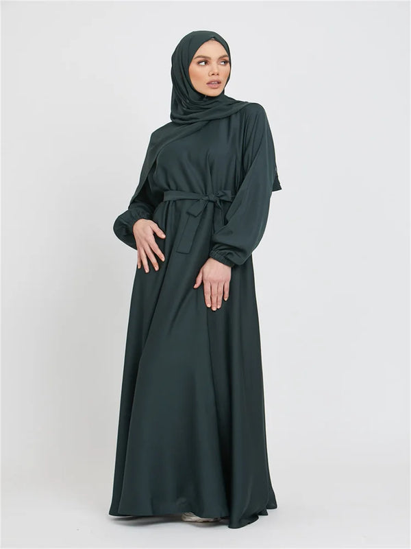 A woman wearing a dark green Moroccan style kaftan abaya with a hood and tie waist.