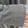 Gros plan sur la manche d'une caftan abaya fluide gris avec broderie de perles blanches et argentées complexes.