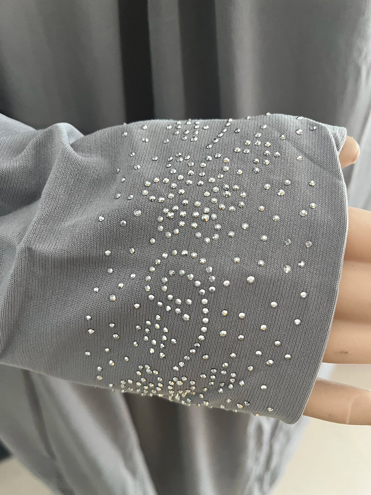 Gros plan sur la manche d'une caftan abaya fluide gris avec broderie de perles blanches et argentées complexes.