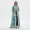 Une femme modélise un trench-coat plissé long, fluide bleu sarcelle et bleu sur une robe noire.