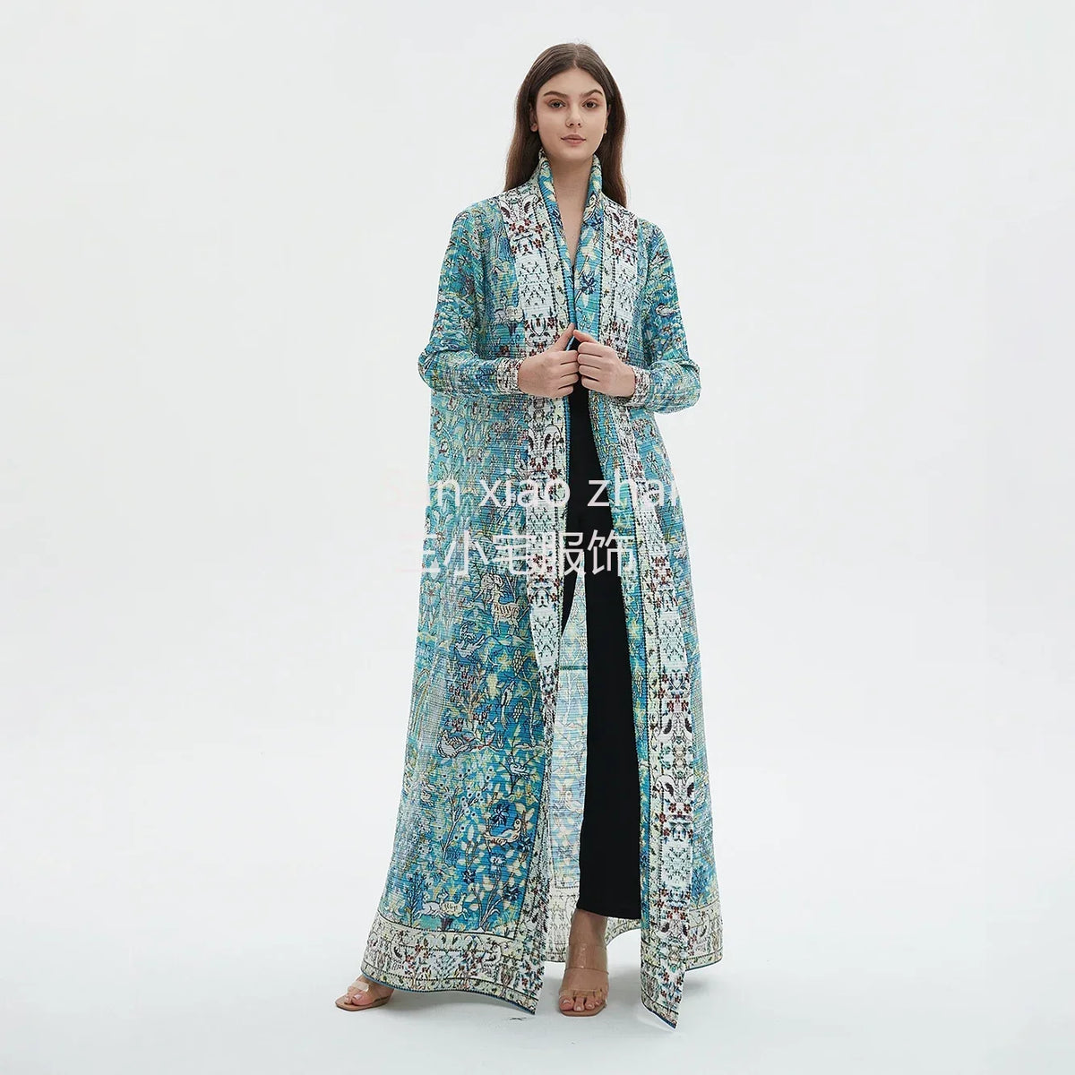 Une femme modélise un trench-coat plissé long, fluide bleu sarcelle et bleu sur une robe noire.