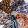 A collection of draped, printed linen hijab scarves in shades of brown, mauve, lavender, and pink.
