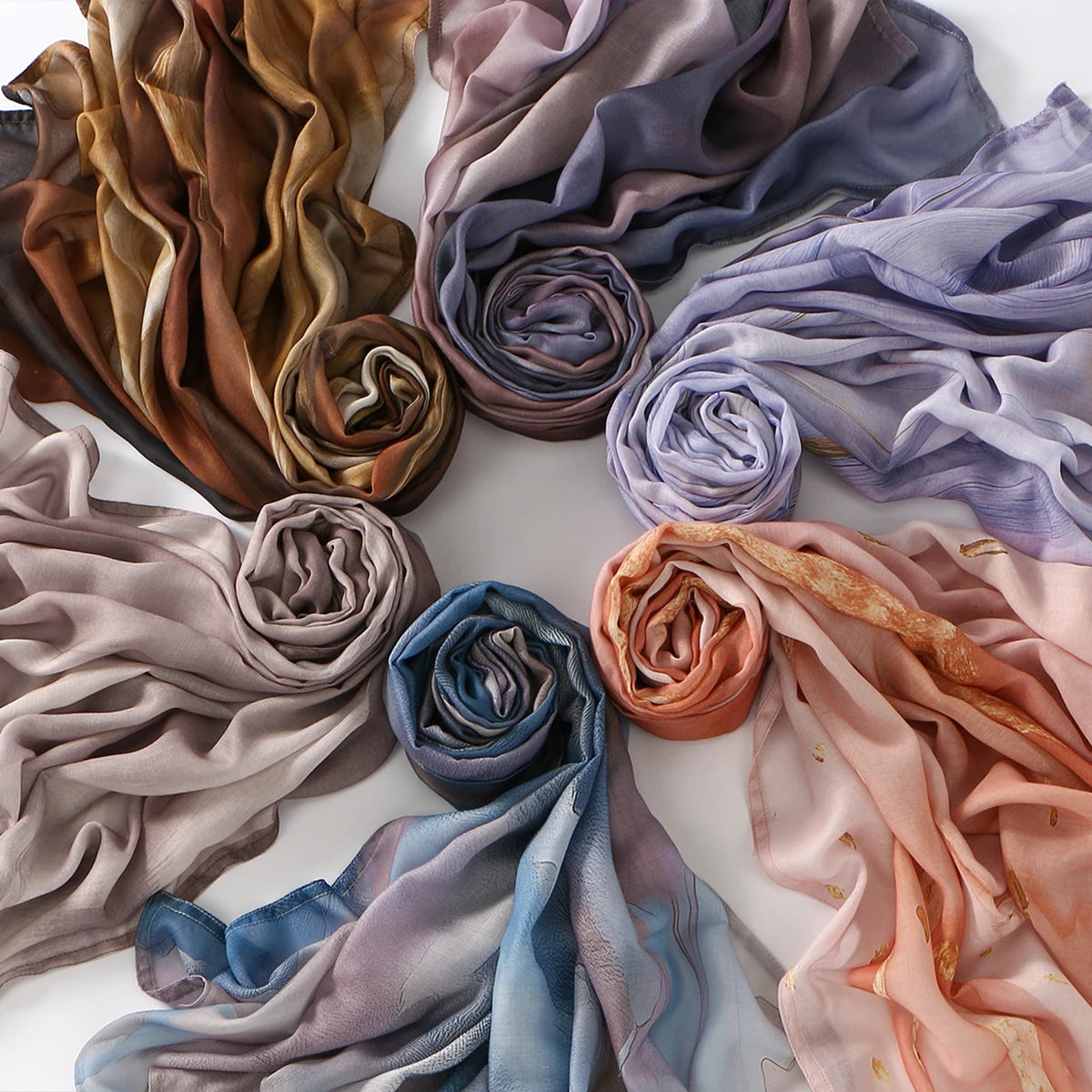 A collection of draped, printed linen hijab scarves in shades of brown, mauve, lavender, and pink.