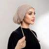 Eine Frau trägt eine beige Hijab-Kappe mit silbernen Strasssteinen und einem schwarzen Samt-Oberteil.
