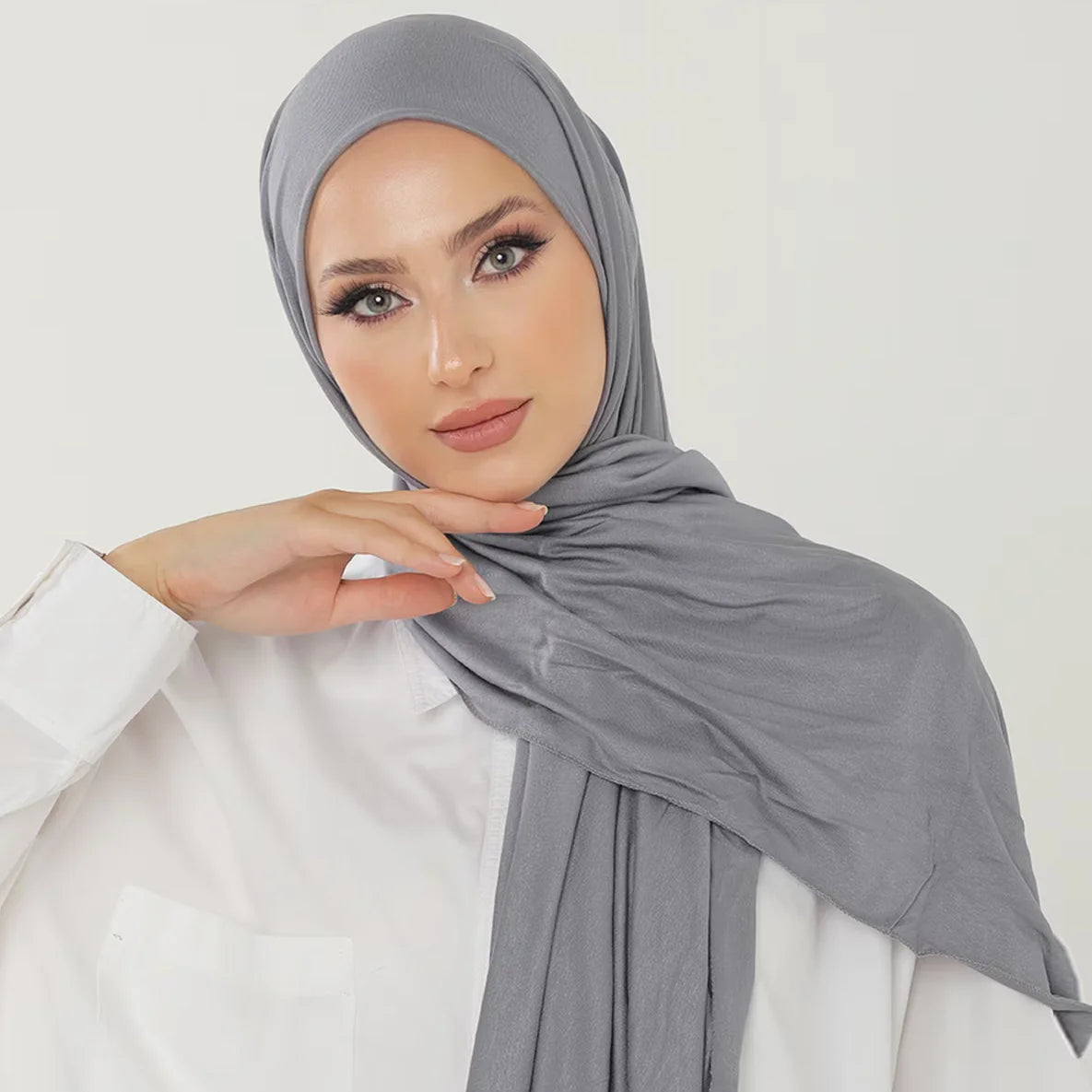 Una mujer vistiendo un pañuelo de hijab de algodón premium gris y elástico con una blusa blanca.