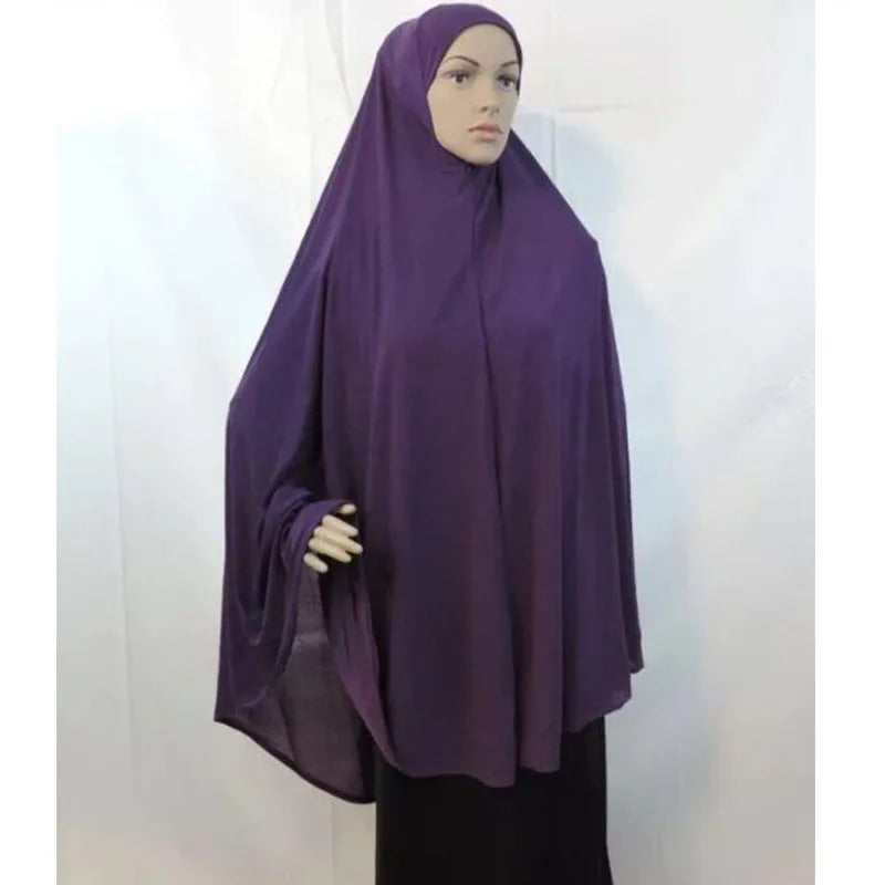 Un pañuelo/hiyab de jersey morado oversize drapeado sobre la cabeza y los hombros de una mujer.