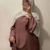 Eine Frau trägt eine mauvefarbene, fließende, lange Abaya mit weiten Ärmeln und einen weißen Hijab und macht ein Spiegelselfi