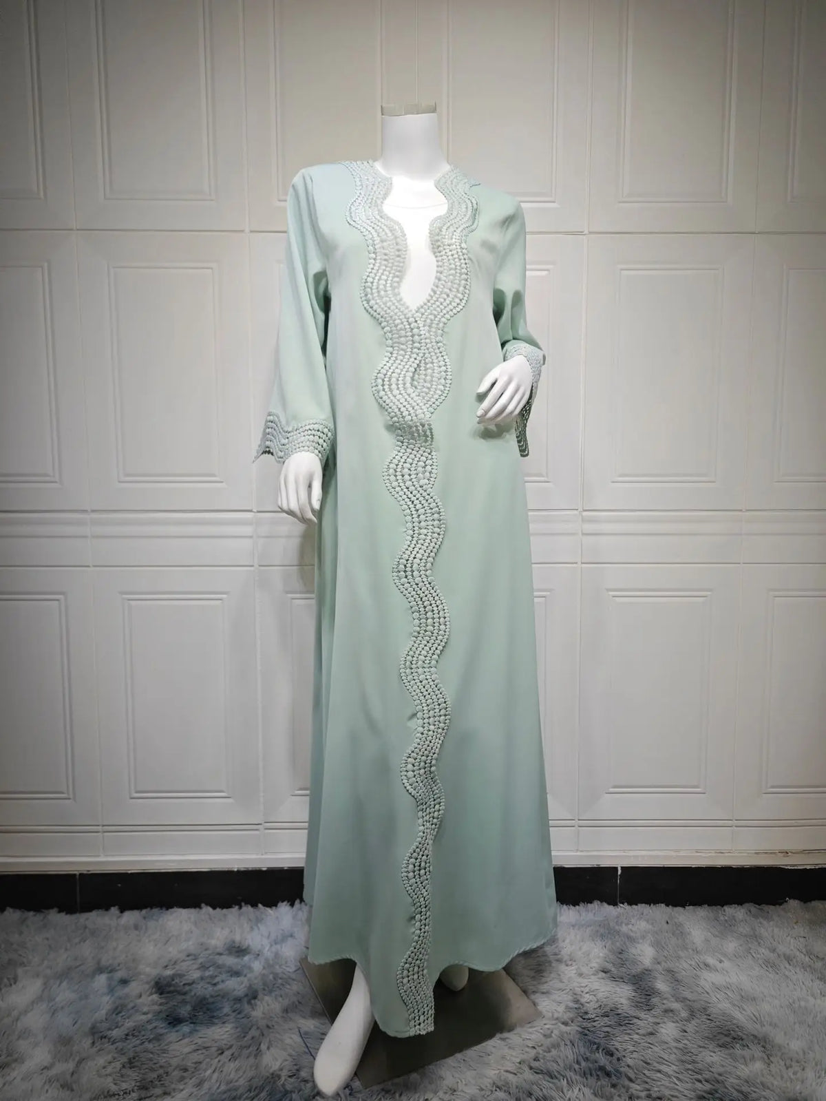 Vestido caftán largo color verde menta claro exhibido en maniquí contra pared blanca con paneles.