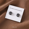 A set of two silver macaron brooches for hijab clips displayed on a white card against a brown fabric background.