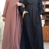 Eine Frau in einem langen, fließenden mauvefarbenen marokkanischen Kaftan-Abaya und eine schwarze Abaya stehen nebeneinander.