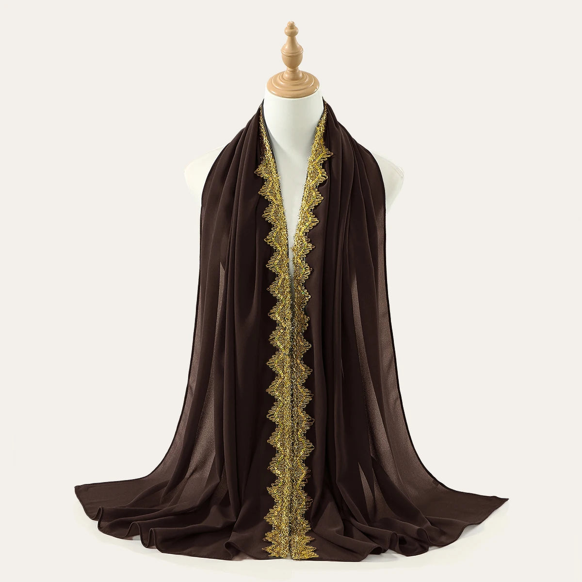 Una bufanda o chal de gasa marrón oscuro con borde de strass dorados, drapeado sobre el cuello de un maniquí.