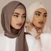 Eine Frau mit brachem Chiffon-Hijab und weißem Oberteil, die für ein Nahaufnahme-Foto posiert.