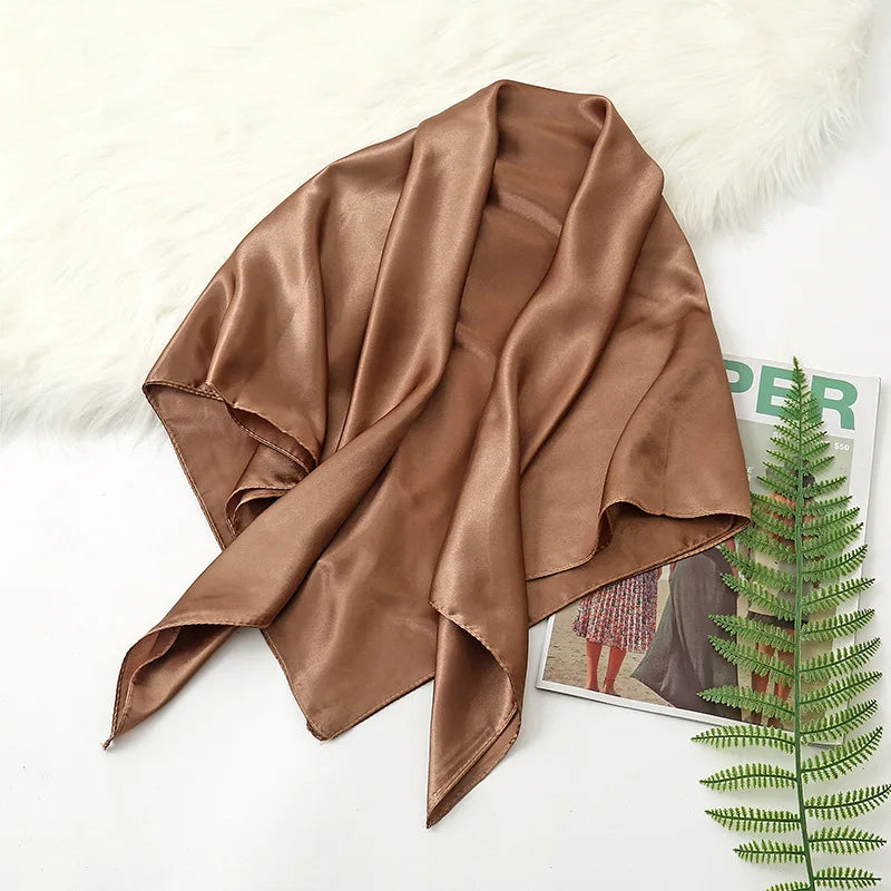 A draped solid brown silk satin hijab scarf resting on a white surface next to fluffy white fur.