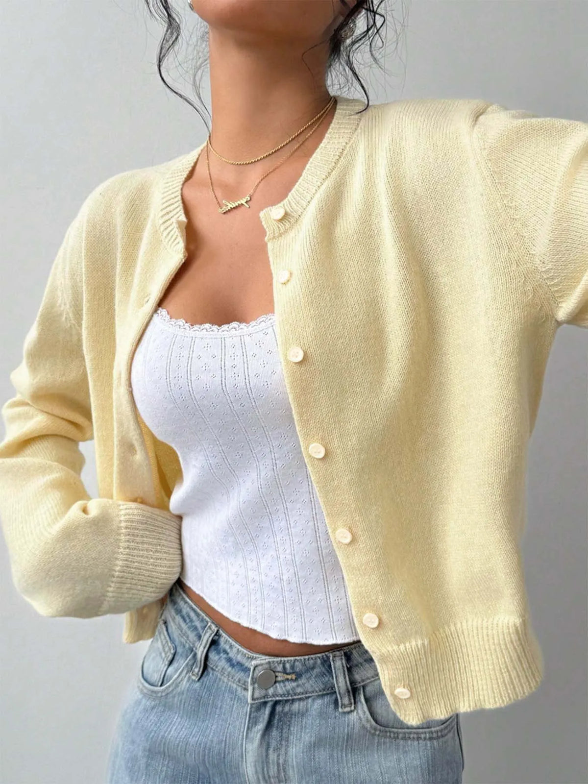 Une femme portant un pull tricoté jaune sur un haut blanc et un jean bleu.