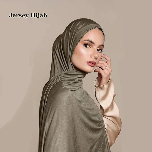A woman wearing a sage green jersey hijab scarf with a high neck and long sleeves.