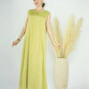 A woman models a lime green flowing modest abaya dress next to a large dried floral arrangement.