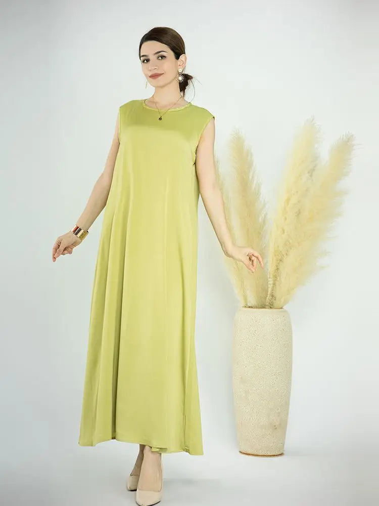 A woman models a lime green flowing modest abaya dress next to a large dried floral arrangement.
