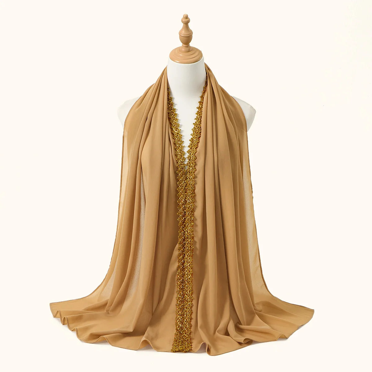 Una bufanda de gasa beige drapeada sobre un maniquí, con un largo adorno de pedrería dorada.