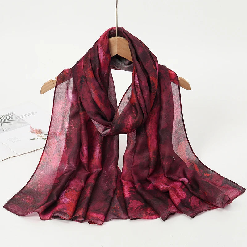 Bufanda de acuarela roja intensa y transparente colgada en un perchero de madera.