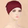 A model wears a deep burgundy stretch jersey turban cap on her head.