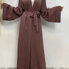 Eine Frau trägt ein fließendes, offenes Abaya-Kaftan in pudriger Rosa mit einer Taillenbinde.