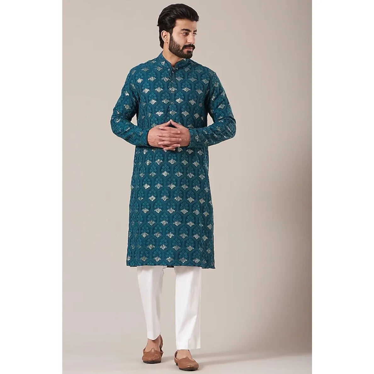 Un hombre vistiendo un jubba thobe tradicional de patrón verde azulado oscuro con pantalones blancos y zapatos marrones.