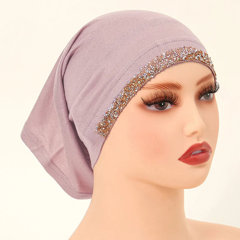 Una modelo lleva un hiyab de algodón modal elástico color rosa empolvado con un ribete dorado brillante.
