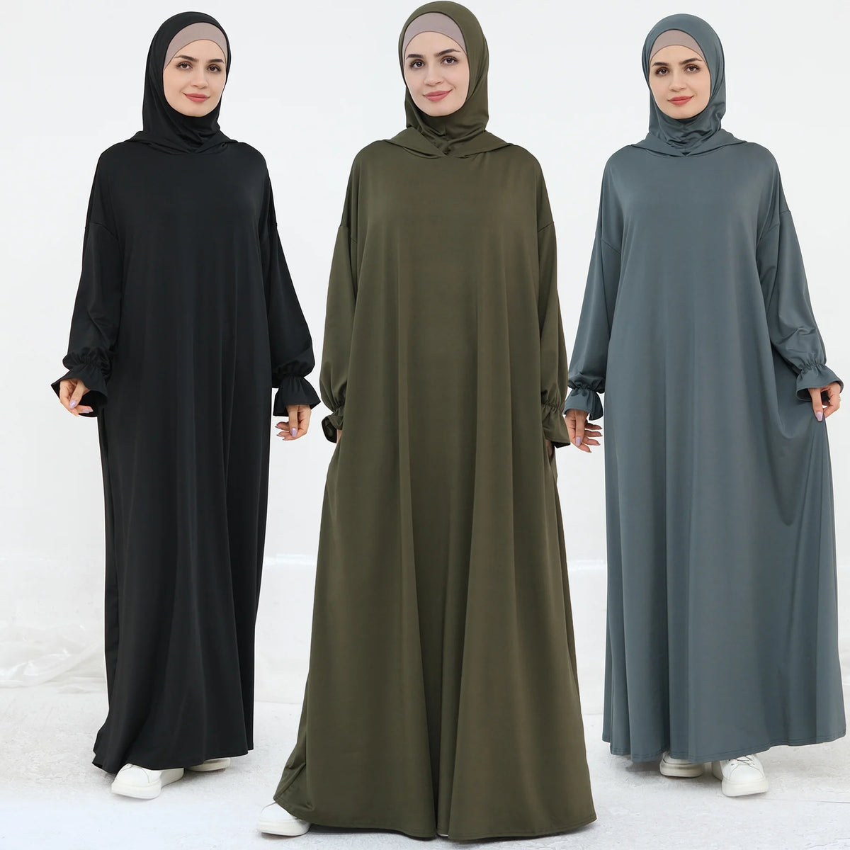 Tres mujeres vistiendo abayas holgadas y fluidas en negro, verde oliva y gris.