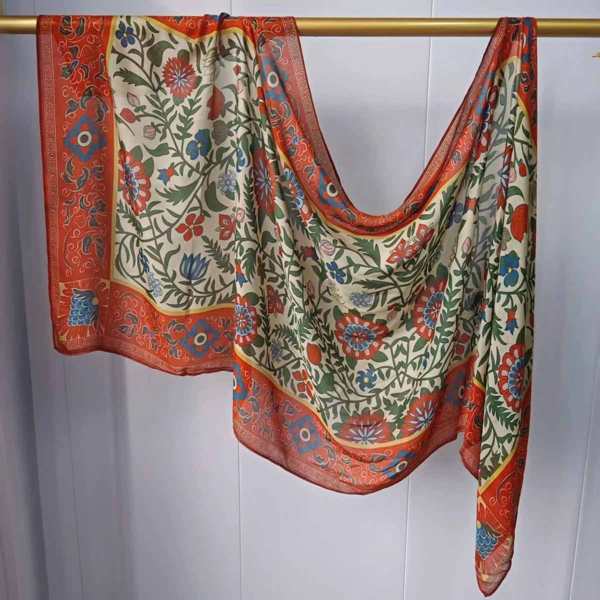 Mehrfarbiger Hijab-Schal mit Blumenmuster in Orange, Grün und Blau, aufgehängt.