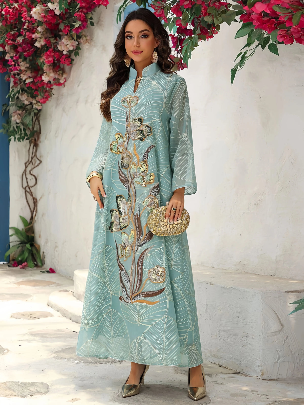 Eine Frau modelliert eine hellblaue, mit Blumenmustern bestickte, paillettenbesetzte Abaya in einer Außenumgebung.