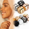 A close-up of a woman wearing a hijab, with various gold and silver macaron brooches displayed nearby.